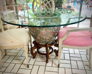 Breakfast table made of giant Chinese planter, stand, and round glass top. Also includes four ivory chairs with pastel seats.