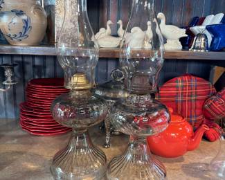 Two clear glass oil lamps with flared fluted bases and one chimney has a flared and scalloped top 18"H