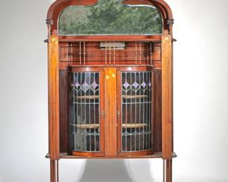 ENGLISH ART NOUVEAU SHOWCASE DISPLAY CABINET | English, late 19th/ early 20th century, manner of Shapland and Petter, leaded glass and inlaid decorations; Carved arch top gallery with pierced openwork whiplash devices, over a shelf with mirrored backsplash, over a barrel-form leaded glass double-door display cabinet framed by two full-length open supports inlaid with tulip decorations in contrasting woods, all raised on four straight inlaid decorated and openwork-carved legs
l. 45 x w. 14.5 x h. 78 in.
