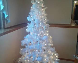 Christmas tree. Approximately 6.5 feet tall with white decor. Located in basement
