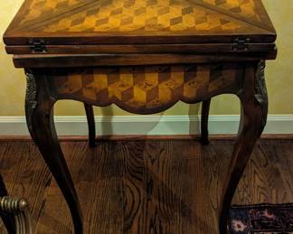 Italian handkerchief games table in the Louis XV taste, executed in mahogany, burl, rosewood, and leather, having a parquetry inlaid four part top opening to reveal a leather covered playing surface with integral four chip wells, surmounting a wide bombe' apron with conforming inlay and one drawer, the whole rising on cabriole legs with gilt metal mounts and sabots, 30"h x 21"sq; open 36"sq.