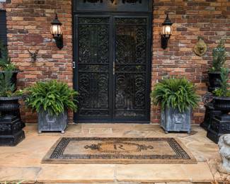 Very inviting front door area, with pair of lead-finished square planters, with pinecone finials and fleur de lis details, pair of concrete spaniels, pair of cast iron squatty planters on stands, with handles, pair of tall cast iron urns on stands. Both sets of cast iron planters are freshly planted with annual begonias and a tall evergreen.