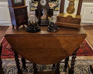 One of three antique English oak barley twist side drop-leaf tables, with clocks, watch display cases and salesmen's sample furniture chest.