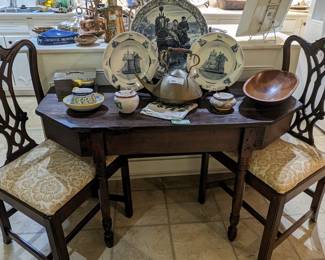 Antique drop-leaf table with pair of vintage Chippendale style side chairs, blue/white Delft plates, wooden dough bowl, brass teapot and Portuguese pottery. 