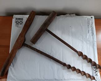 Two rustic barn beam augers. The T-handle of the bigger one is 14 inches wide and the drill is 15.5 inches long. The smaller auger has a T-handle that measures 7.75 inches wide. That second drill is 13.75 inches long.