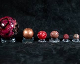An assortment of spheres: Four small Rhodochrosite spheres, a Copper sphere, and a larger pink and black Rhodochrosite sphere. All come on clear plastic stands. Largest sphere dimensions are included.
