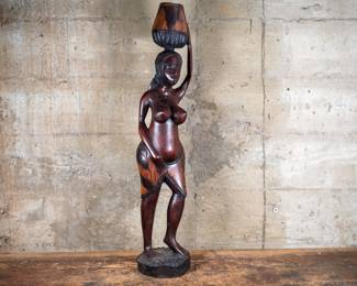 A wood carved statue of an African woman carrying a basket or pot on her head. Originating from the Congo.

