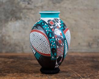 A beautiful pottery vase with colorful painted and geometric designs. Made by artist Oscar Quezada Jr. for Mata Ortiz. This vase has a pointed base, and rests on a black braided ring base.
