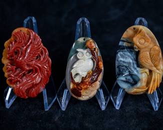 Three pendants made out of carved Jasper depicting an owl, a parrot, and a phoenix.
