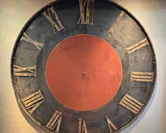 Antique Large Round  Clock Face. 

Late 19th / early 20th century; circular face –two (2) halves riveted on center line, painted cinnabar-red and black, cast metal Roman numerals bolted to face. Lacks revolving pointers or “hands,” likely old repaint to center disc, abraded black outer ring, flaking numerals paint, minor areas of rust – primarily near numerals “VI” to “VII.”