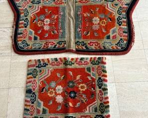 Rugs – saddle, two-piece set, hand knotted wool pile on cotton foundation

Likely Tibetan, second-quarter 20th century

Features a rectangular and butterfly shapes, floral on red-orange field, rainbow lishui stripes capped with ruyi heads border; butterfly canvas lining deteriorated on edges and faintly ink stamped INDIA AUST 1952

Measures: 23 inches by 27 ½ inches and 30 inches by 57 inches.
