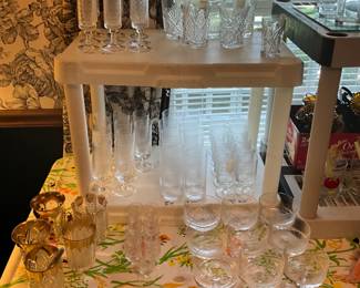 Left to right- top - set of glasses (9), various size glasses & designs on right; bottom shelf - 3 different size glasses sets with same pattern; on table to left - gold rim glasses (5) all different, set of 9 matching dessert cups