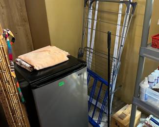 This corner of the sale has a small refrigerator and a folding drying rack. Look carefully, there is a manual rug sweeper.
