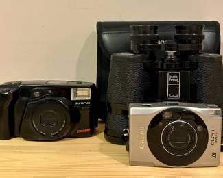 Olympus Camera (left), Bushnell Binoculars (back), Canon GLPH Camera (front)