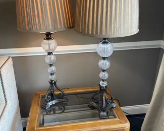 Pair of lamps with metal base and glass on top of wood and glass side table