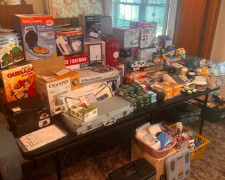 This is a table FILLED with excellent little measures for the home! The left side of the table is filled with small kitchen appliances interior original boxes, and the right side is filled with loads of medical, health & beauty and more! 