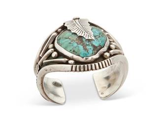 260
A Southwest Silver And Turquoise Cuff Bracelet
Mid-20th century
Appears unmarked
A chunky silver cuff with central set turquoise and silver feather overlay motifs and triangular wire edges
6.75" total inner C x 2.625" H, with a 1" gap
124.8 grams gross
Estimate: $500 - $700