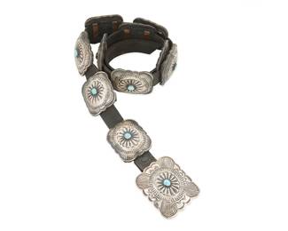 247
A Navajo Sterling Silver And Turquoise Concho Belt
Mid/late 20th century, Diné
Buckle stamped: L / Sterling
A belt with ten darkened sterling silver rectangular conchos and a matching buckle, each with repoussé center, stamping and central set turquoise and all mounted to a black leather strap
Buckle: 2.75" H x 3" W; Each concho: 2.25" H x 2.5" W; Strap: 41.25" L x 1" H
500.3 grams gross
Estimate: $600 - $900