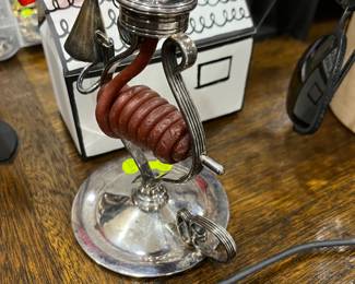 A silver plated wax jack which holds its original coil of sealing wax. It would have sat on a writing table to be used when adding a personal seal to letters and official documents by melting the wax and then impressing it with a patterned seal. This one is Spanish and has its snuffer attached by a chain. c1900.