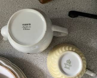 Bottom side of white textured tea cup and tea pot, multicolored floral design and gold detail 