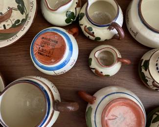 Bottom side of collection of white tea set, painted scenes of quaint neighborhood 