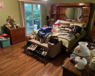 Bedroom full of wood furniture, upholstered loveseat with hidden storage, women's clothing, purses and beauty + self-care products. 