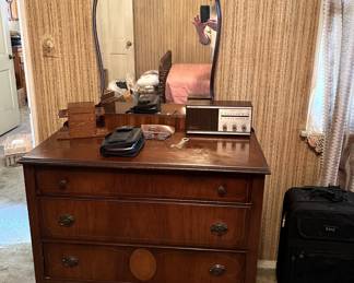 This is a very nice mirrored dresser, along with a radio and a piece of luggage to the right.