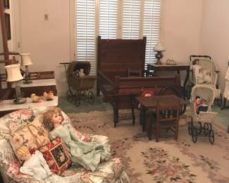A room filled with antique child’s furniture, prams, dolls, toy chests, and charming period accessories. 