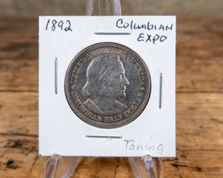 A 1892 50C Columbian Exposition commemorative half-dollar. Good toning, estimated AU condition.