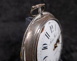 A silver pocket watch in a silver case with an enamel face and Arabic numerals, made by watchmaker John Ward of London, Late 18th Century. The movement on the back is signed "John Ward Fore Street London" Number 2690. The back movements shows a monogram of King George III, with two "G"s one reversed, and the Roman numerals III with a crown affixed on top. This watch is missing it's glass cover, and has a damaged hinge and watch hand.
