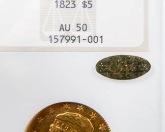 An 1823 $5 Capped Bust Half-Eagle Gold Coin. Graded an AU-50 by NGC. This coin also has a CAC Gold Sticker, meaning CAC believes the quality of the coin may warrant a higher grade. It is estimated there are 80 to 100 surviving examples of this coin. The design features are well brought up in most areas. The semi-reflective green-gold surfaces display pleasing coral color near the peripheries.