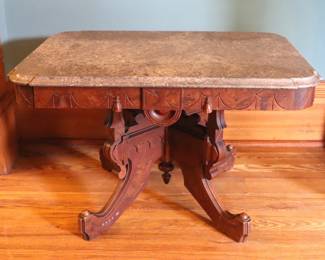 A 19th century Victorian Eastlake Period coffee table. Walnut construction with Burl detail, shaped Marble top and conforming apron over a carved stretcher base with scrolled legs. Table was shortened, older finish with some wear, shrinkage, losses to applied carvings. 30 x 22 x 18 3/4" high overall. ESTIMATE $300-400 NOTE: This lot picks up from the home in Coldwater, Michigan.