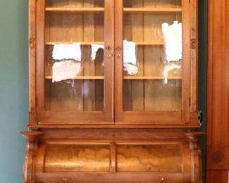 A 19th century Victorian Period roll top secretary. Walnut construction with figured panels features a carved floral crest over an upper bookcase section with glass pane doors and three interior shelves, on a lower section with cylinder roll which opens to reveal a fitted interior and pull out writing surface, flanked by two candle stands over three long dovetailed drawers with applied carvings and bracket base. Older finish with wear particularly at sides, minor shrinkage and joint separation, repairs and some losses to molding, leather writing surface curled at edges, drawers unlocked but lacks key. 46 x 22 3/4 x 106" high overall. ESTIMATE $400-600 NOTE: This lot picks up from the home in Coldwater, Michigan.