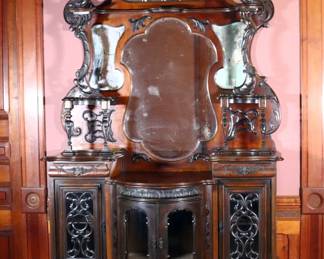A 19th century Rococo Revival etagere. Mahogany construction features a pierced crest over a scrolled back with four shaped mirrors, applied foliate carvings and upper shelf, on a breakfront lower section with central bow front cabinet and fretwork detail flanked by two side cabinets with short dovetailed drawers above glass pane doors and applied carvings, terminating in a shaped lower shelf with cabriole legs and raised pad feet. Refinished with minor wear, shrinkage, and damage, small repairs and losses to applied carved details, losses to silvering of mirrors. 55 x 14 x 102" high overall. ESTIMATE $800-1,200 NOTE: This lot picks up from the home in Coldwater, Michigan.