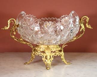 A turn of the century Rococo style Crystal center bowl. Cut Crystal bowl in a Gilded Bronze frame with two Phoenix form handles on a pierced base with scrolled legs. Gilded finish with minor wear and oxidation, replaced Crystal bowl with a few micro-flakes to edge, lacks rings or small element at handles. 17 x 8 x 11" high overall. NOTE: This lot picks up from the home in Coldwater, Michigan.