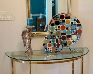 Brass and glass console supports an angel candleholder and a pair of Peggy Karr fused art glass plates reflected off gold framed mirror.