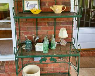 Green painted metal bakers' rack holding pottery and outdoor decor.