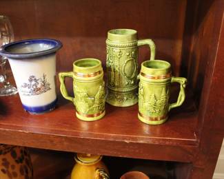 Set of three vintage green beer steins shown with a flared white and blue ceramic flared vase