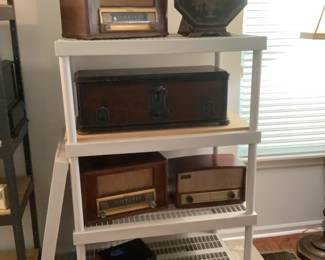 Two silver tone radios, second shelf is a radio with speaker sitting on top shelf, then two more radios
