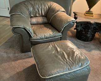 Large over stuffed leather chair with cream color piping and ottoman.