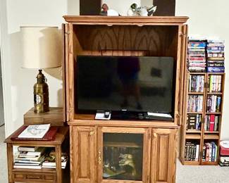 Upright entertainment center, flatscreen TV, Vintage side table, many books, DVD's, VHS's, duck decor
