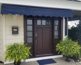 Spectacular entry door with two side lights; fixed awning; potted ferns