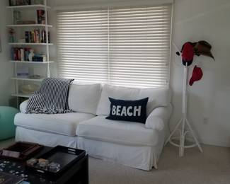 Cozy white slipcovered couch; wicker coat tree; blinds