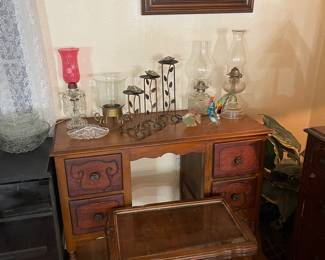 antique knee-hole vanity, small display/side table, antique hurricane lamps, and other glass decor