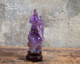 A Chinese carved Amethyst Buddha sculpture mounted on a wooden base. Traditional detailed carving with two smaller figures above Buddha holding a cloth sack.