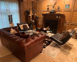 Faux Knoll Barcelona Chair (B), Faux fur decorative pillows ,Leather chesterfield loveseat ,  Faux Knoll Barcelona Chair (A), Decorative woven leather pillows , Upholstered club chair , Abercrombie Leather Rhino Footstool , Abercrombie Leather Hippo Footstool , African Tribal Seated Couple Sculpture, Stone pedestal 