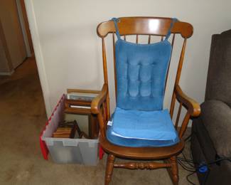 Picture frames, and plastic bin, along with a comfortable chair, that rocks, also known as a rocking chair.