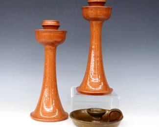 Three 20th century Jugtown Pottery candlesticks.  Includes a pair of flared candlesticks with mottled Orange glaze and a chamberstick with mottled Green/Orange Accidental glaze.  Impressed "Jugtown Ware" marks, candlesticks also dated "1982".  A few small flakes, chamberstick with some surface wear.  Up to 6" diameter and 12" high.  ESTIMATE $50-100