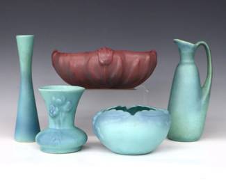 Five pieces of 20th century Van Briggle Art Pottery.  Includes a slender bud vase, a baluster form ewer, flared vase and floriform rose bowl with "Ming" Blue matte glaze, and an oval scalloped vase with flower frog insert and Mauve/Purple matte glaze.  Incised Van Briggle marks with "Colo. Spgs." and various numerals.  Some surface wear and crazing, minor discoloration, Mauve vase with hairline to bottom.  Up to 8 3/4" long and 9" high.  ESTIMATE $100-150