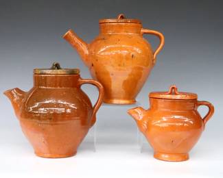 Three 20th century Jugtown Pottery teapots.  Bulbous forms with lift-off covers, strap handles and mottled Orange glaze.  Impressed "Jugtown Ware" marks.  Crazing, some flakes, one spout with small chips, one with painted underside.  6" to 7 3/4" high.  ESTIMATE $50-75
